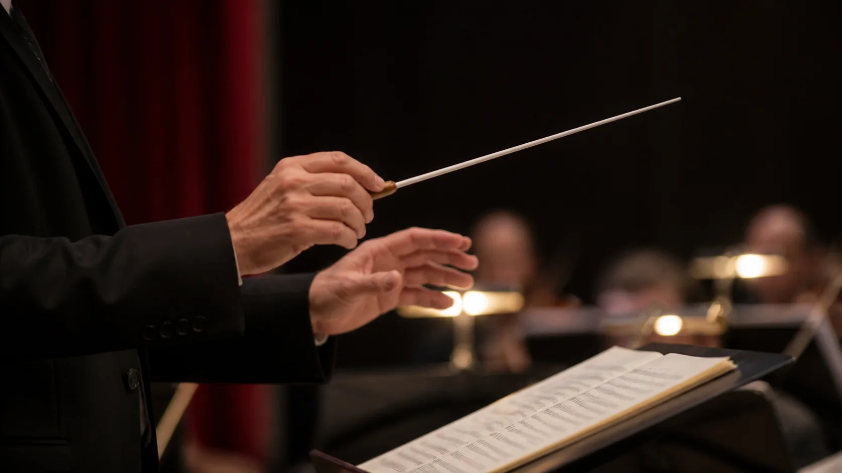 Mãos de um maestro conduzindo com batuta diante de uma partitura